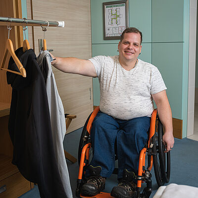 Rollstuhlfahrer hängt Jacke auf an absenkbarer Kleiderstange